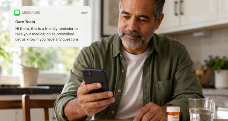 Patient sitting at the table at home, looking at a message from the Care Team, reminding the patient to take their medicine. On the table, there is a notebook, paper, pen, medicine bottle and a glass of water. The patient is sitting in their kitchen.
